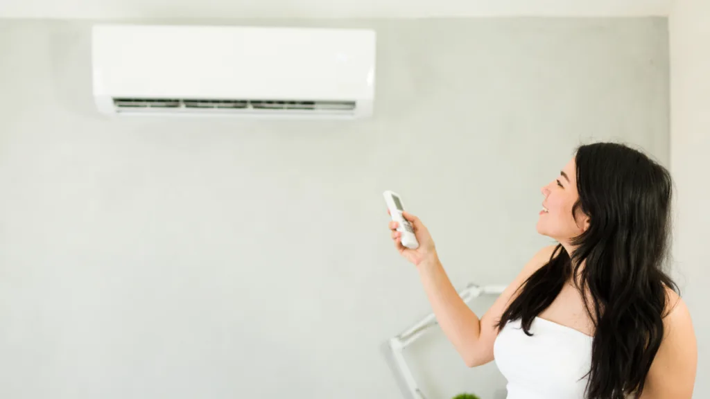 A woman adjusting the temperature on a ductless mini split ac unit with a remote control