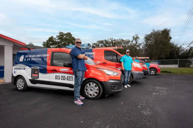 Custom Air Conditioning Air Quality team members stand proudly beside their branded service vans parked outside the companys office ready for AC repair and service calls