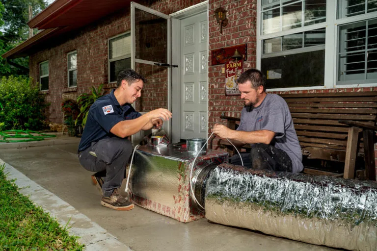Two Custom Air Conditioning Air Quality technicians work on sealing an insulated air duct with metallic tape
